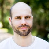 Headshot of a man with a beard wearing a white t-shirt outdoors with a blurred green background